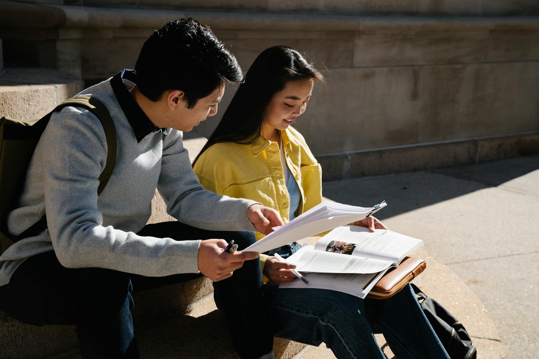 Dwójka uczniów uczy się razem na dworze, czytając książki i notatki