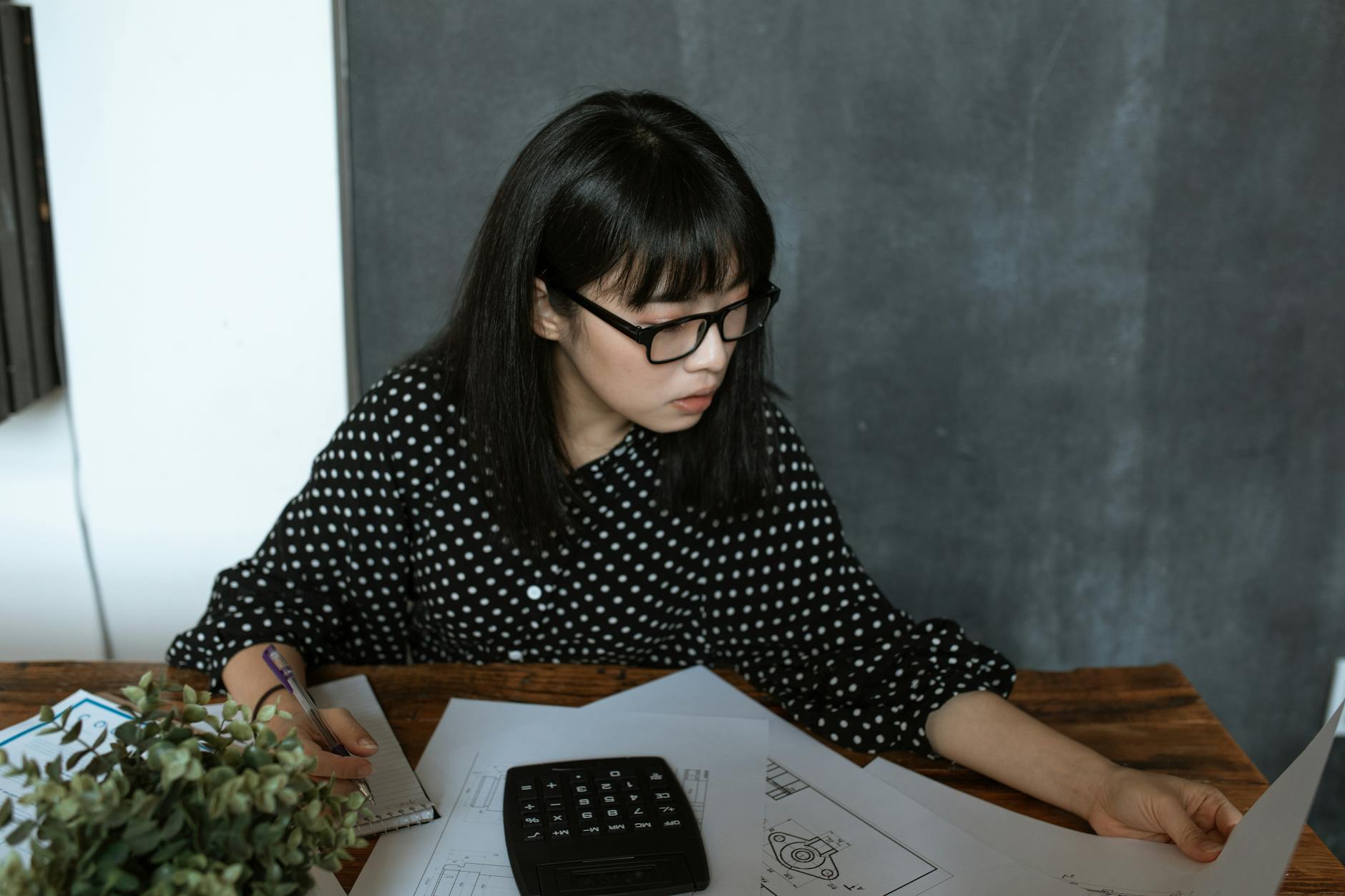 Azjatka w okularach analizuje dokumenty finansowe z kalkulatorem