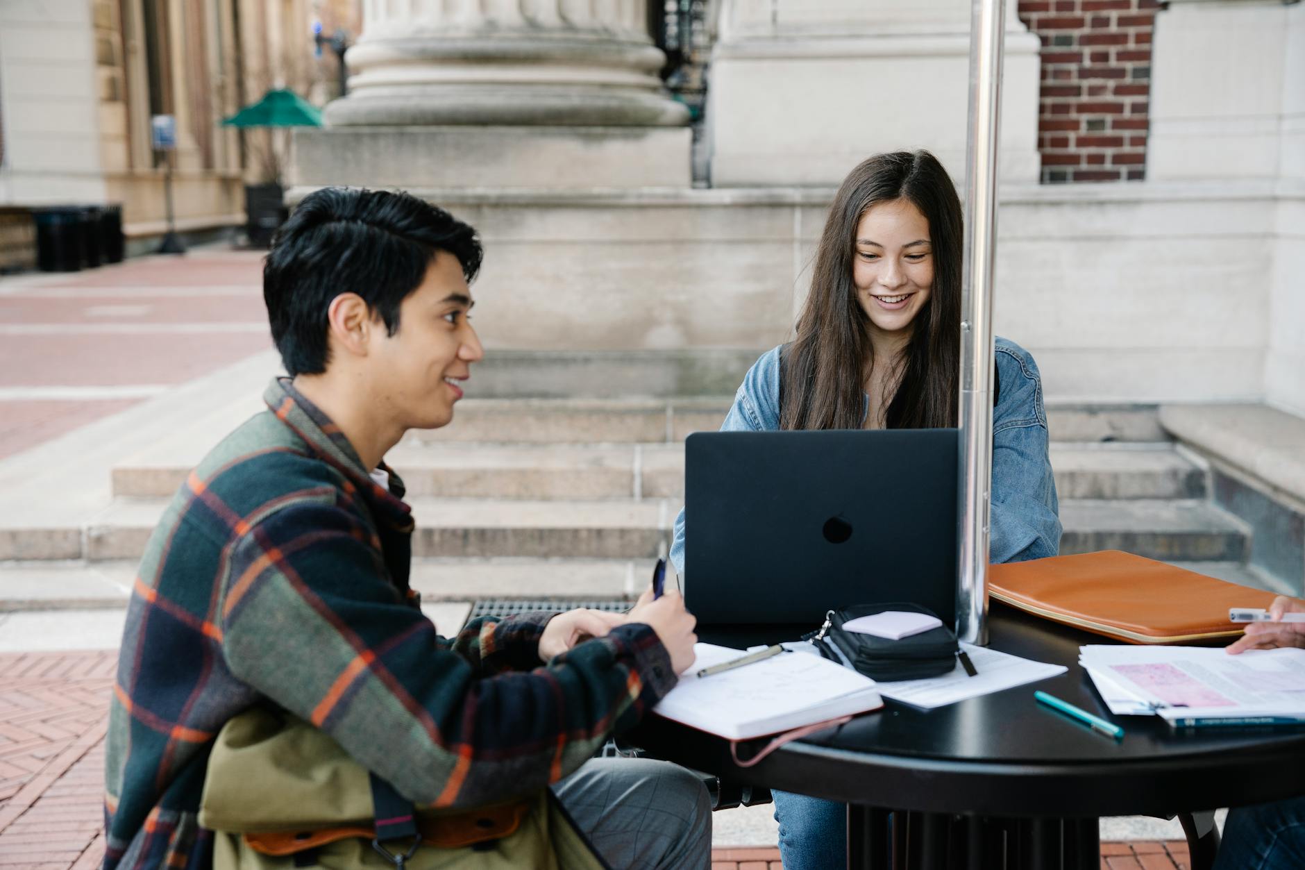 Dwóch studentów przy stoliku na zewnątrz pracuje na laptopach