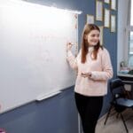 Nauczycielka języka angielskiego pisze na białej tablicy w klasie