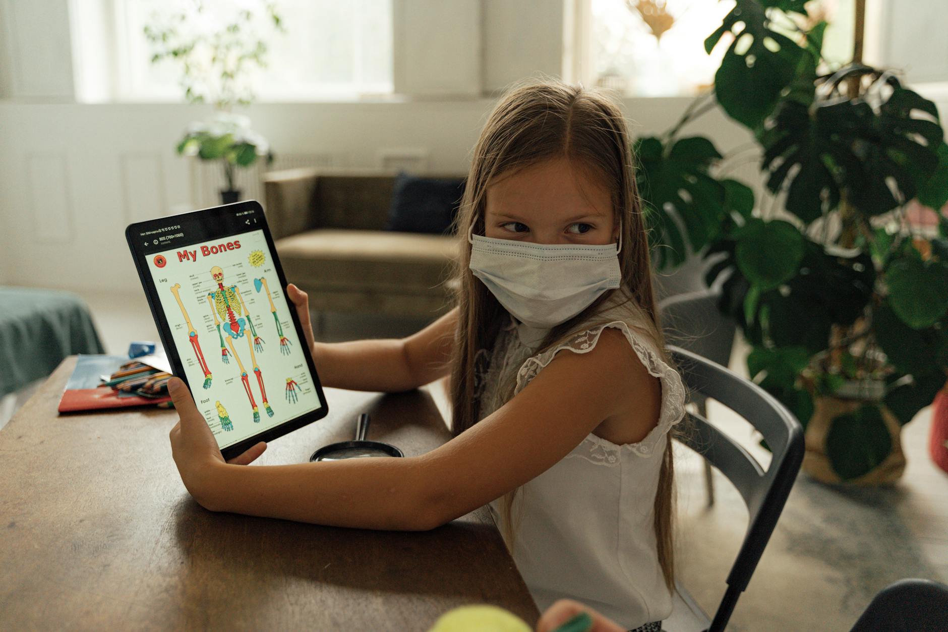 Dziewczynka w maseczce korzysta z tabletu w domu