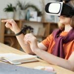 Nastolatek w goglach VR uczy się w domu przy stole z materiałami szkolnymi